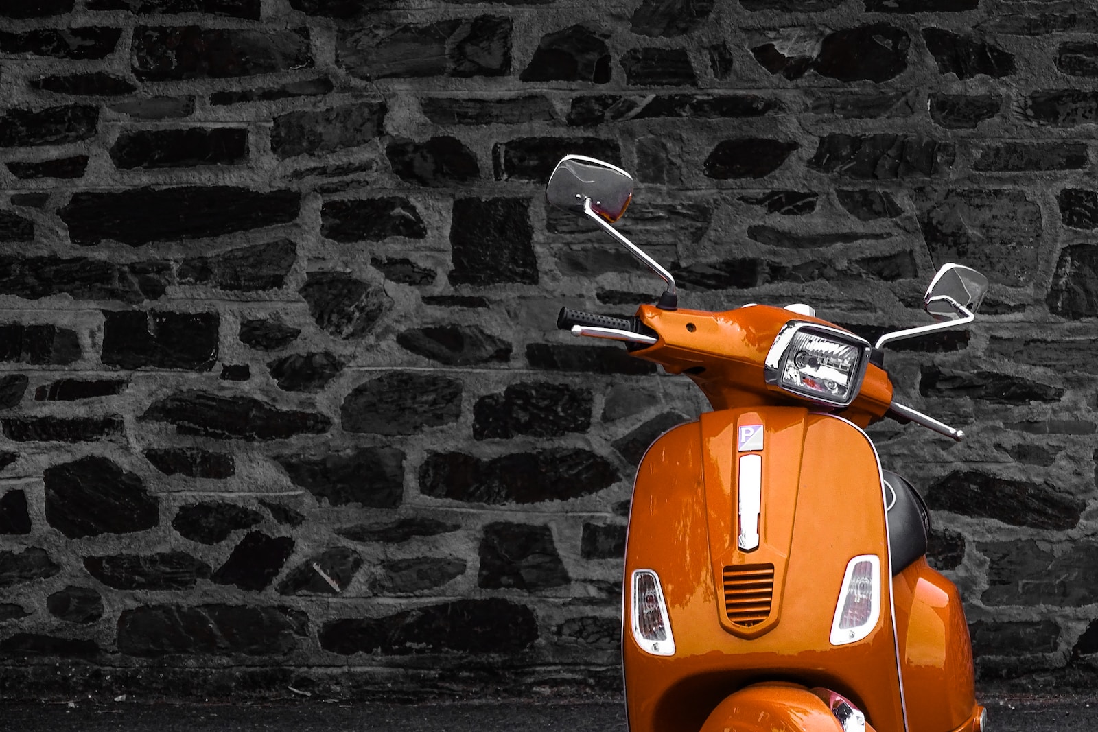 orange motor scooter parked beside black and white wall